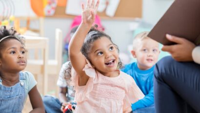 Little girl raining her hand to answer a question.