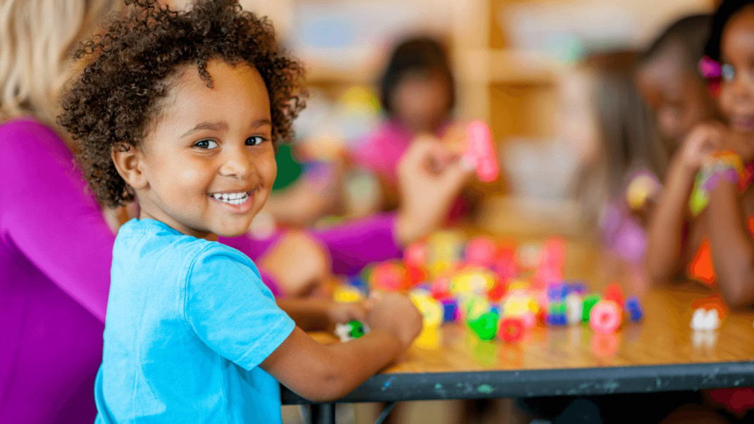 Young boy wearing a blue shirt smiling and playing at a table.