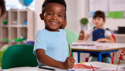 Child in a blue shirt smiling and painting a picture.