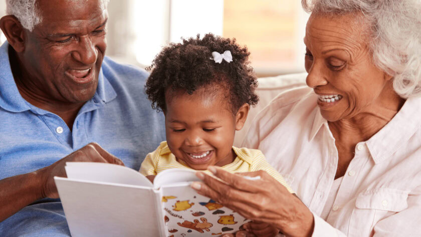 toddler reading a book with grandparents